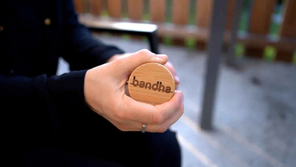 Detailaufnahme einer Hand, die eine Trinkflasche mit einem runden Holzelement mit dem gravierten bandha Logo hält.