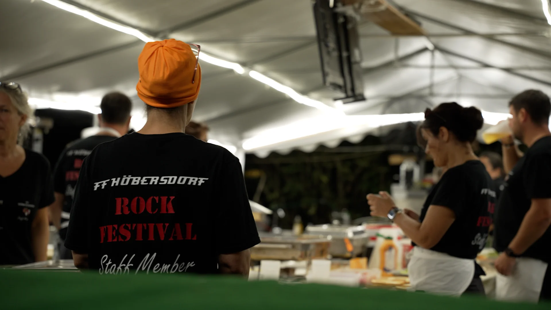 Screenshot aus einem professionellen Eventfilm von ArsMotion für ein Rock Festival: Authentische Momentaufnahme von Personal mit gebrandetem T-Shirt im Catering-Bereich zur Stärkung des Employer Branding.
