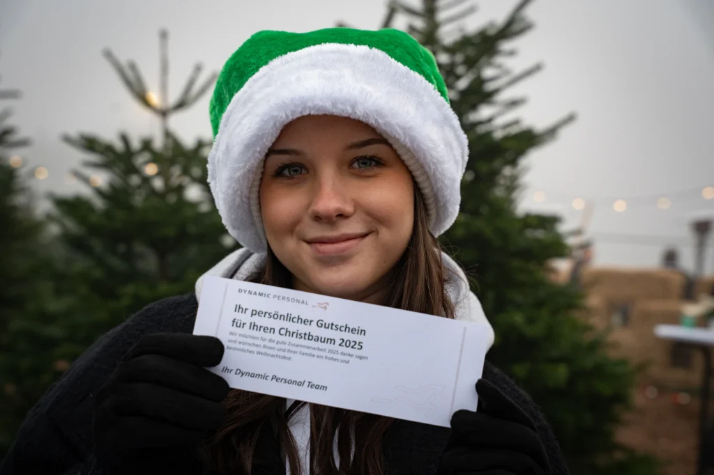 Sympathisches Mitarbeiter-Portrait mit Weihnachtsmütze und Gutschein – fröhliche Eventdokumentation der Dynamic Personal Weihnachtsfeier.