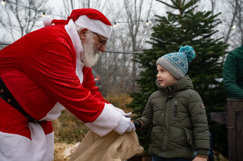 Besuch vom Weihnachtsmann beim Dynamic Personal Event: Geschenkübergabe an ein Kind beim Christbaumservice Traiskirchen – emotionale Eventfotografie.