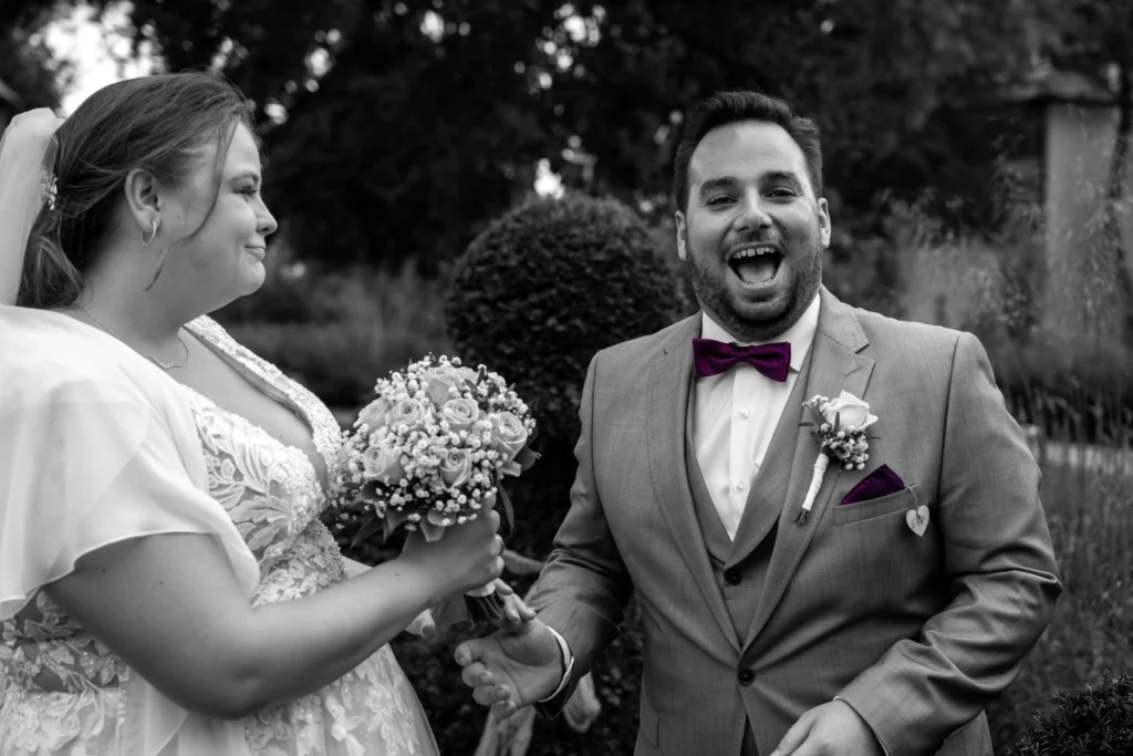 Emotionales Hochzeitsfoto mit Color-Key: Schwarz-Weiß-Aufnahme des herzlich lachenden Bräutigams Patrick mit farblich hervorgehobener lila Fliege, während Braut Eileen ihn anlächelt.