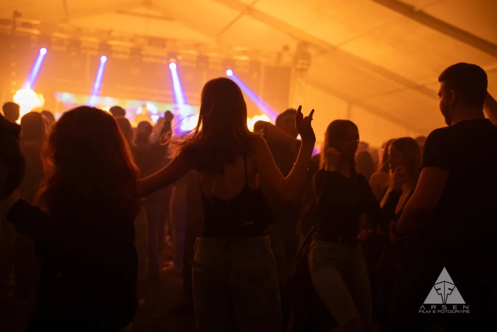 Atmosphärische Eventfotografie beim Greenfield 2025: Tanzende Menge in warmem Bühnenlicht in Kleinhadersdorf