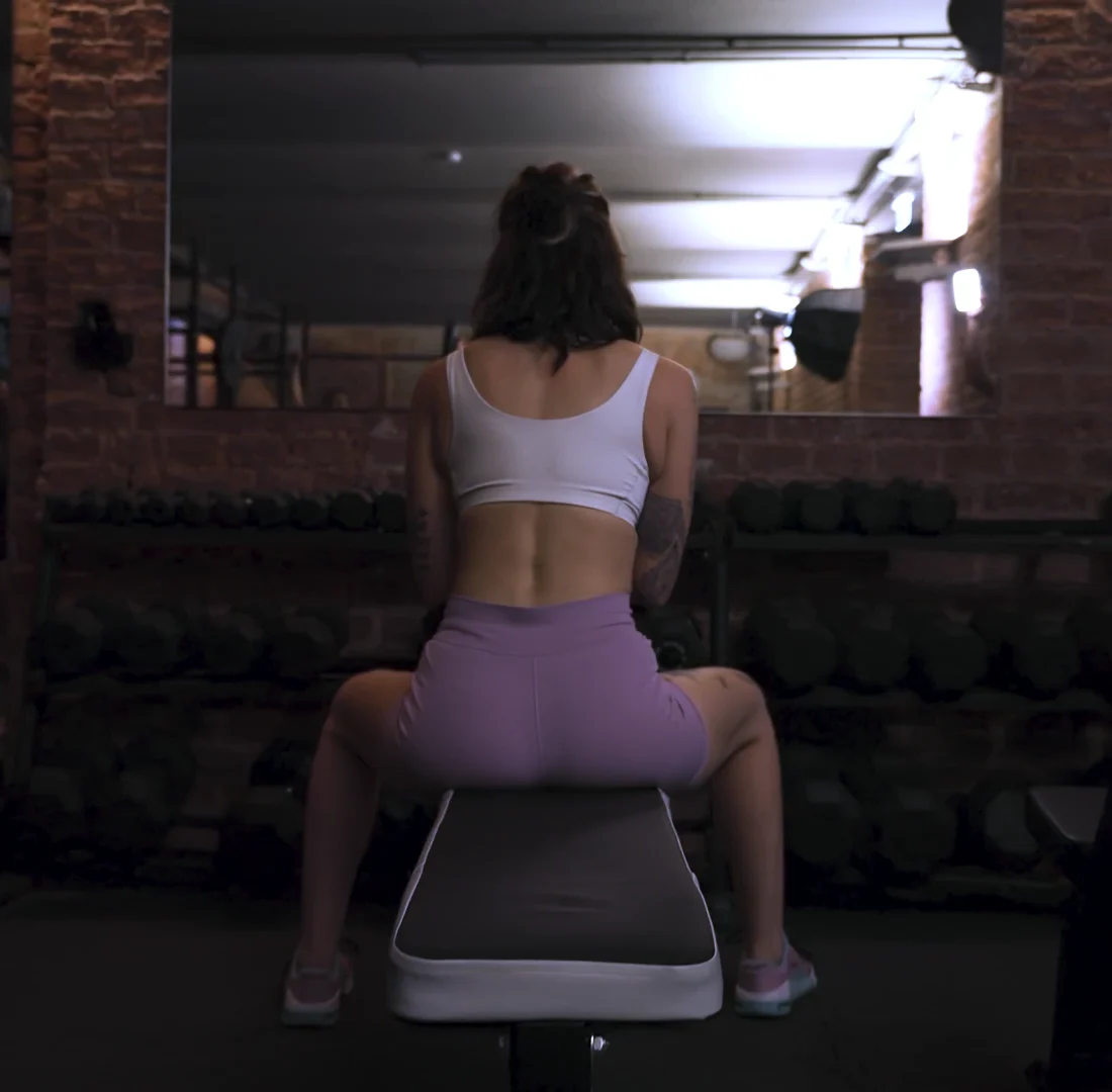 Ines Gruber sitzt fokussiert auf einer Hantelbank in einem dunklen Fitnessstudio in Wien