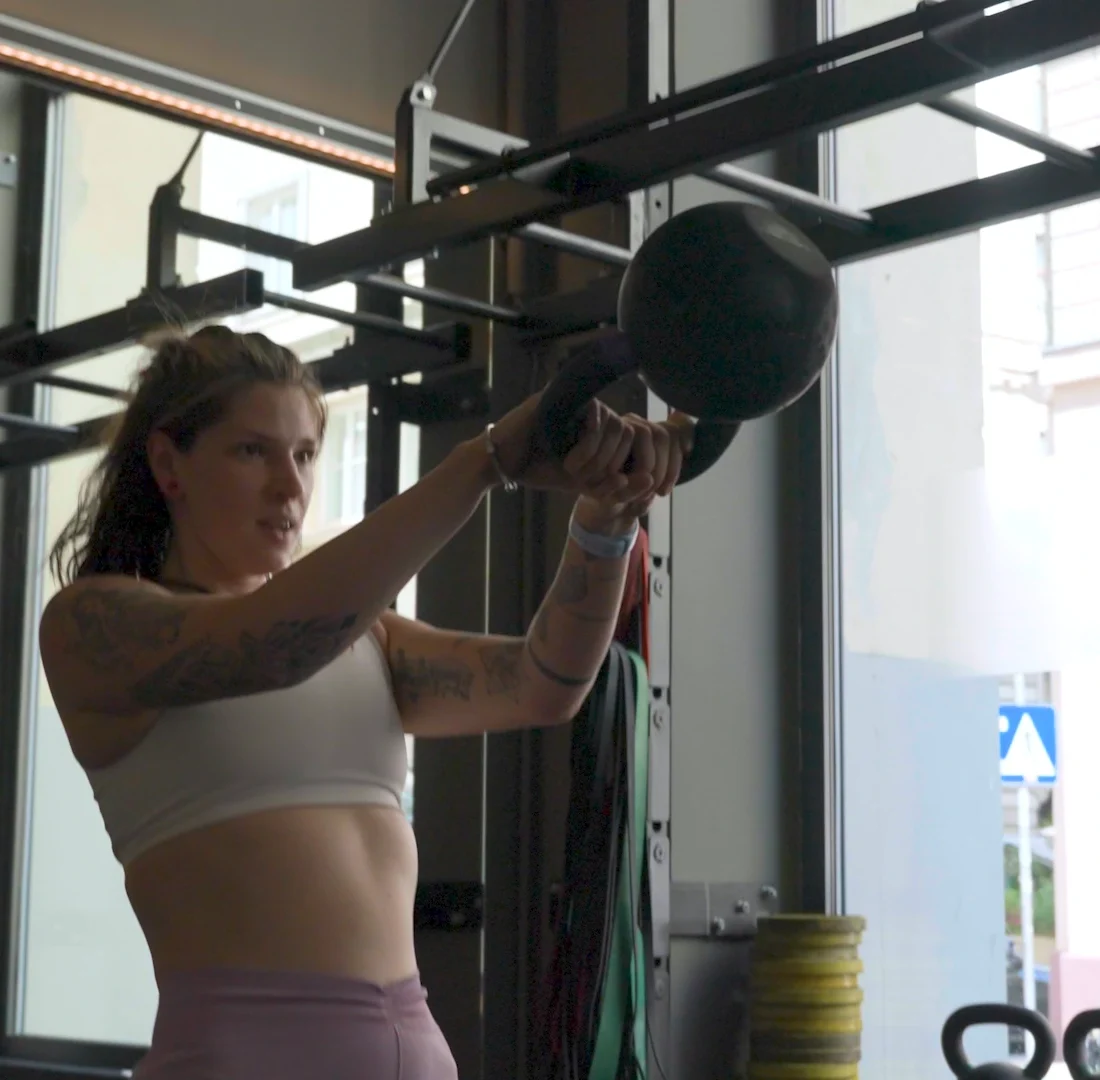 Fitness Coach Ines Gruber bei der Ausführung von Kettlebell Swings vor einem hellen Fenster