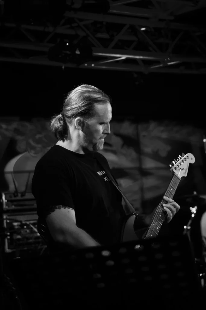 Atmosphärische Konzertaufnahme: Gitarrist der RainbowKissers im Fokus vor dunklem Hintergrund – professionelle Event-Dokumentation.