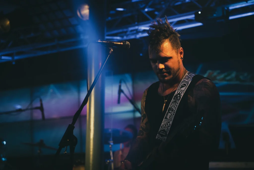 Konzertfotografie eines RainbowKissers-Musikers mit Gitarre auf der Bühne unter blauem Scheinwerferlicht.