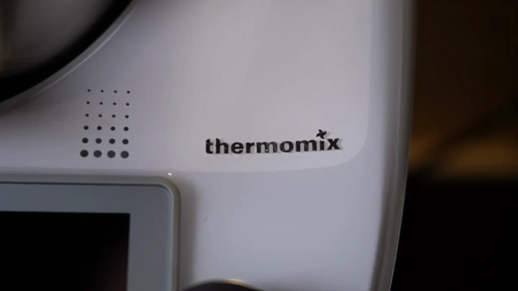 Detailaufnahme des weißen Thermomix TM6 Geräts mit scharfem Fokus auf das graue "thermomix" Markenlogo.