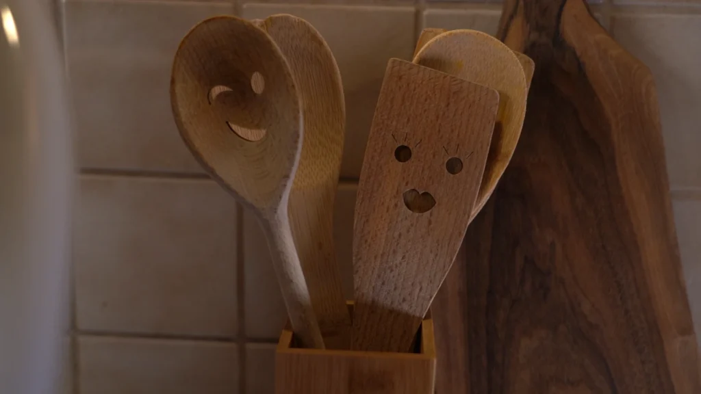 Atmosphärisches Küchendetail: Zwei Holzkochlöffel mit eingeschnitzten Smiley-Gesichtern stehen in einem Halter vor einer Kachelwand.