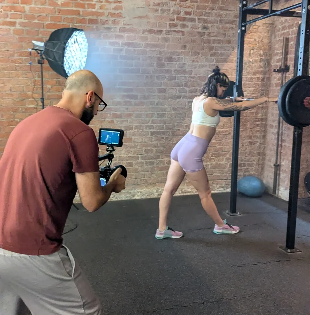 Totale des Filmsets im Fitnessstudio: Videograf filmt Ines Gruber mit professionellem Licht-Setup vor einer Ziegelwand
