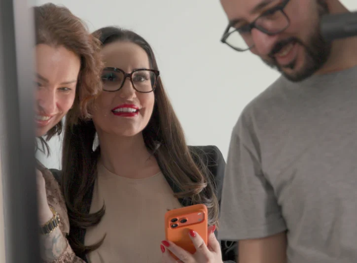 Mediengestalter Arsen Stepanian und Dijana von Dynamic Personal sichten gemeinsam gut gelaunt die ersten Ergebnisse des Videodrehs auf einem Smartphone.
