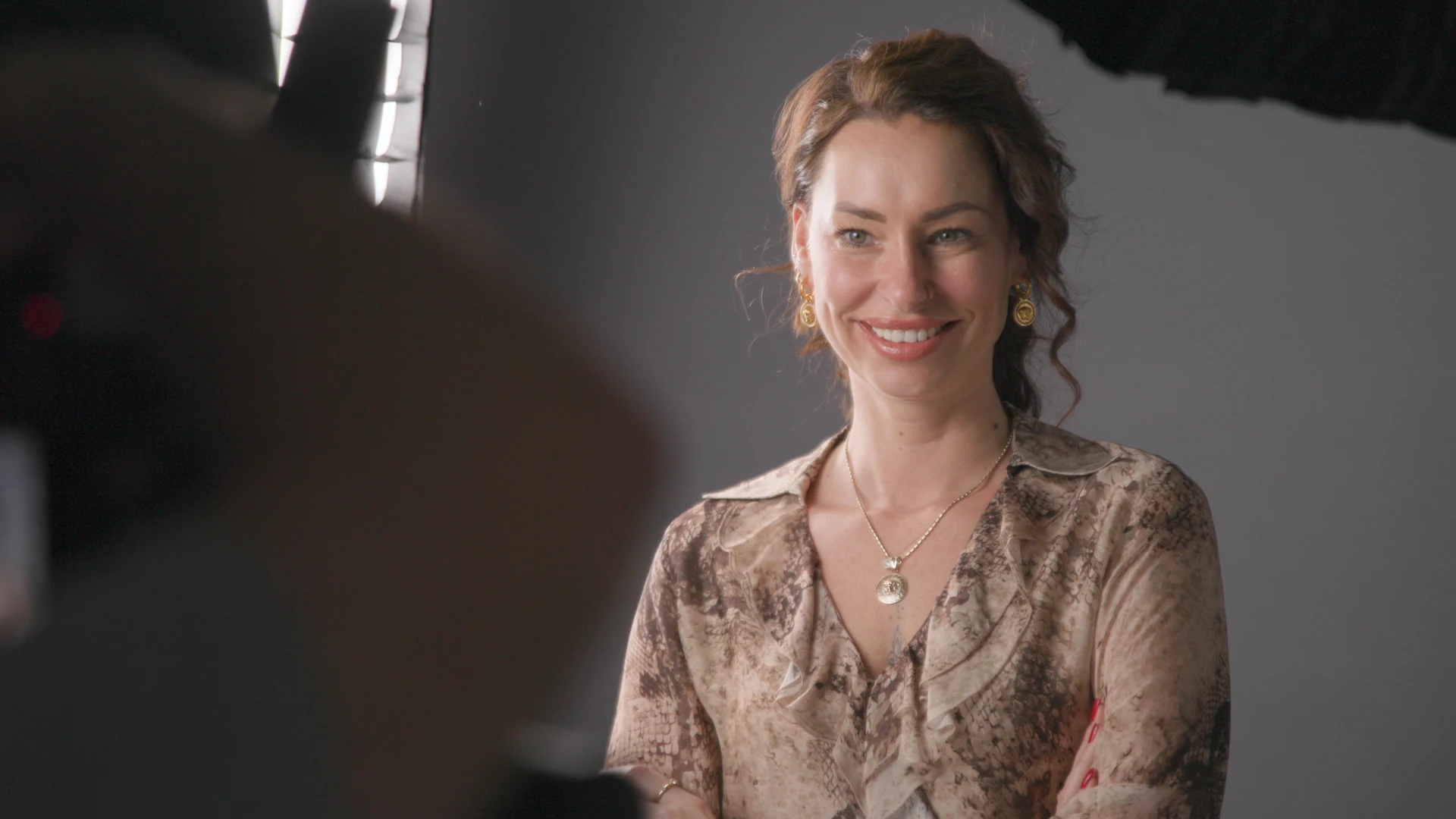 Ein Porträt der lächelnden Edina, Mitarbeiterin bei Dynamic Personal, in einem Fotostudio mit professioneller Beleuchtung. Sie trägt eine gemusterte Bluse und dezenten Goldschmuck.